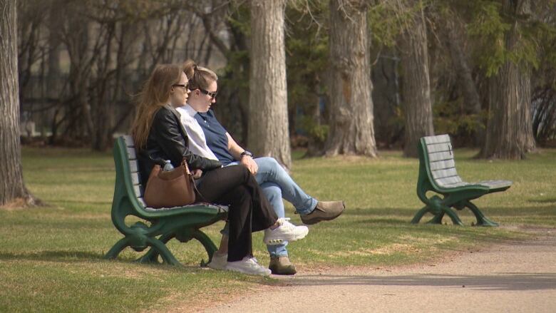 Two women can be seen sitting on a bench in a park in Saskatoon. 