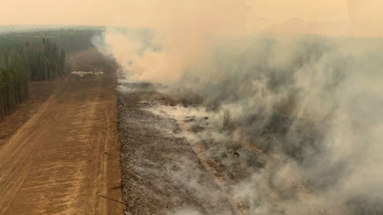 Smoke from a wildfire hangs above a dirt road. 