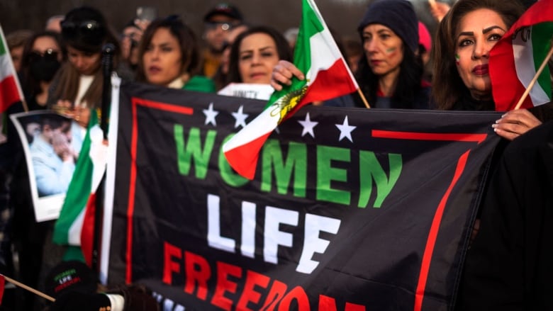 Protestors wave Iranian flags and hold a banner that says 