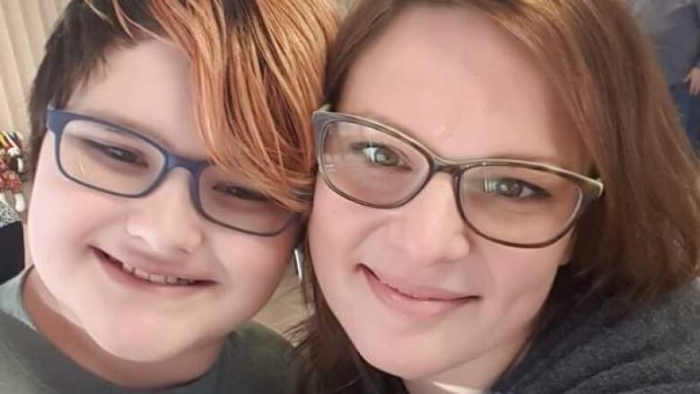 A woman with glasses and her son who also wears glasses smile in a photo. 