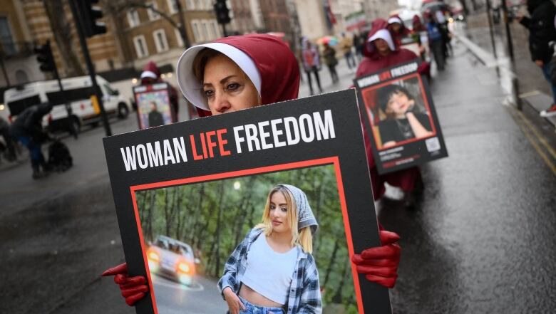 Demonstrators dressed  in red cloaks  and hoods  hold placards reading 'Women, Life, Freedom.'