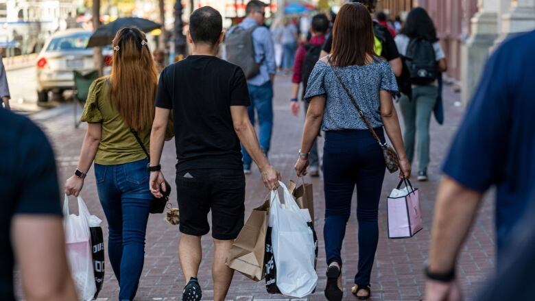 Two women and one man are shown from behind, walking the streets holding shopping bags.