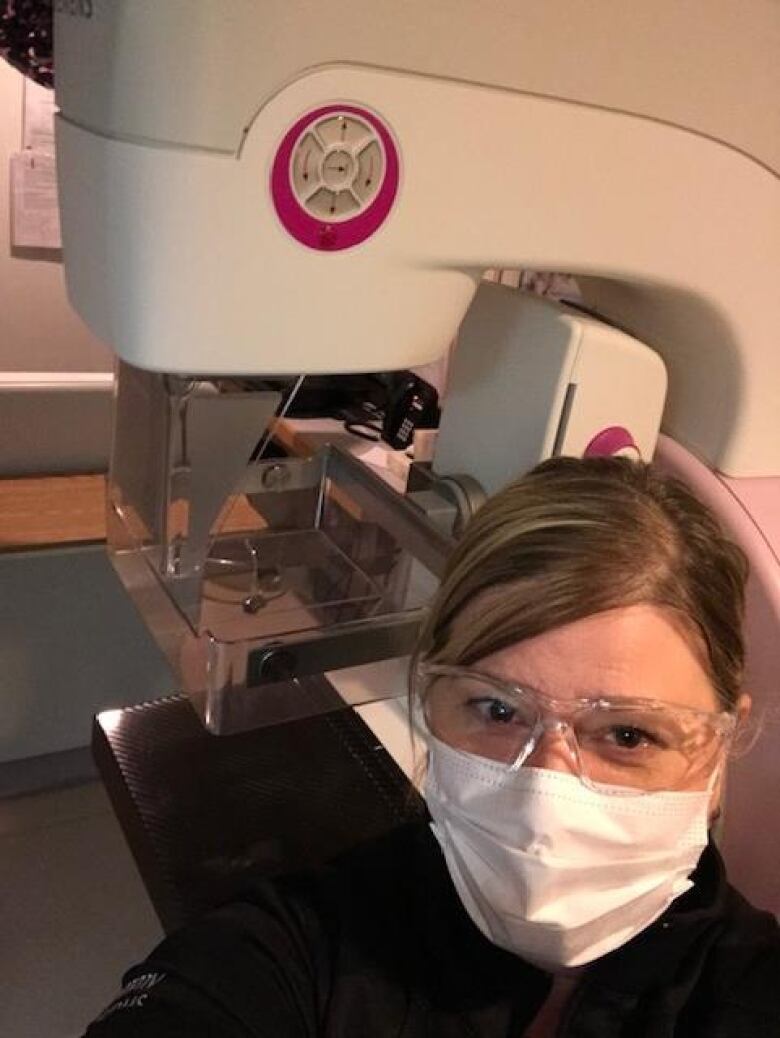 A woman poses in front of a mammography machine.