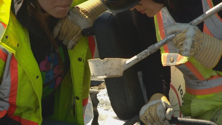 Two city workers inspect a sample of water from a pond. 