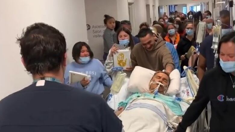 An organ donor lies on a hospital bed and is being escorted down a hallway surrounded by Indigenous relatives.