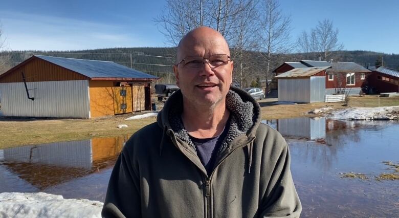 Smiling man standing infront of his front yard. A large amount of water is sitting on his lawn.