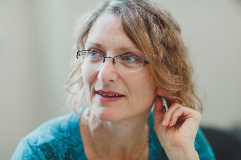 A woman with curly hair and glasses plays with her hair.