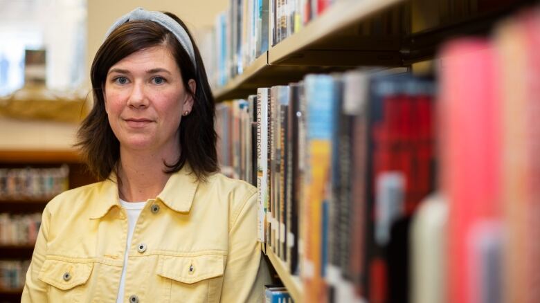 A woman leans on a book shelf.