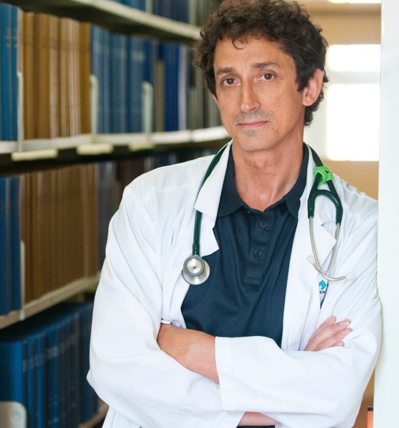 A doctor in a white coat looks at the camera with his arms crossed.