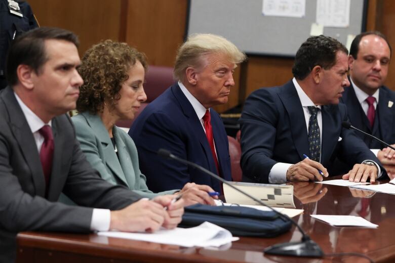 A person sits with their lawyers at a table during a hearing.