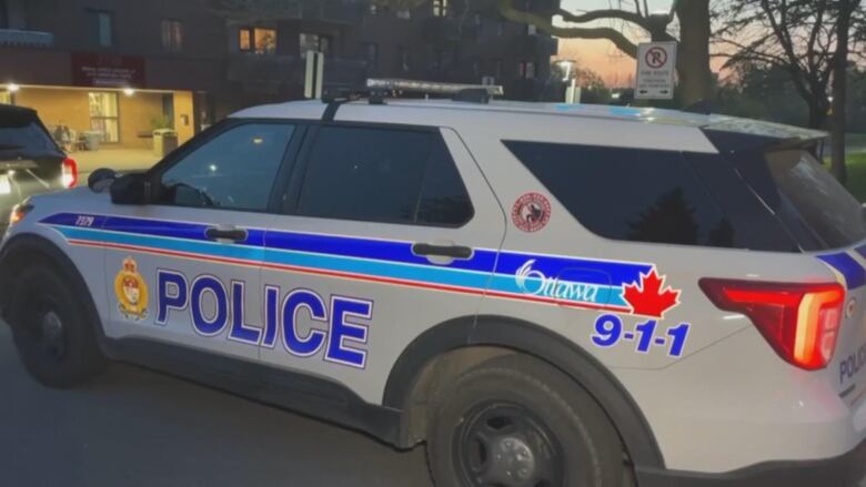 A police cruiser is parked outside of an apartment building. 