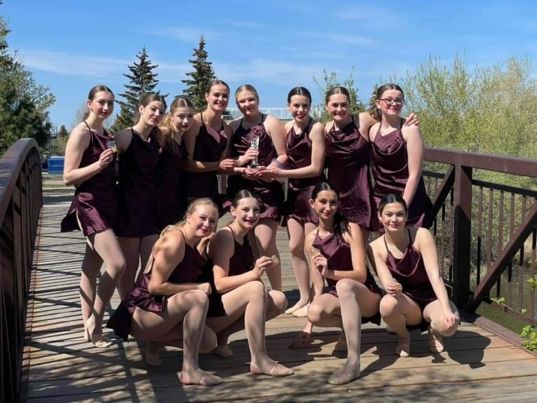 Dancers wearing purple dresses stand together on a small bridge.