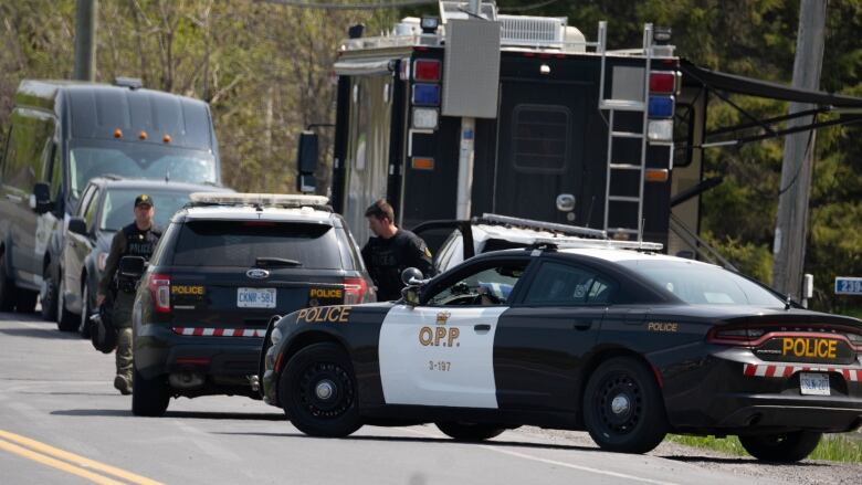 A line of OPP cruisers on a rural street in spring.