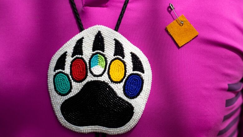 A Moose Hide pin is placed above a Indigenous beaded necklace with a bear paw.