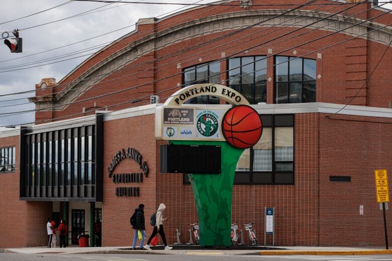 A few people walk in front of a large sports arena.