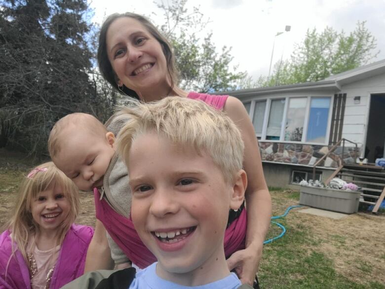 A mother and three kids stand outside a house.