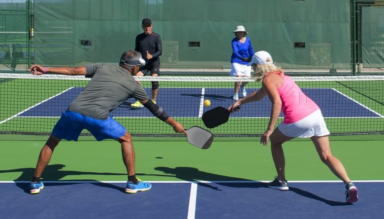 Two pairs of players play pickleball outdoors at a pickleball court.