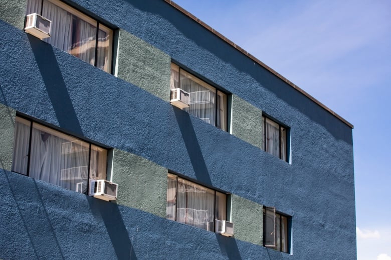 A blue low-rise apartment building in Vancouver's West End has multiple air conditioners hanging out its windows.