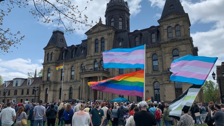 A group of people stand outside a historical building. Several people are carrying large pride flags.