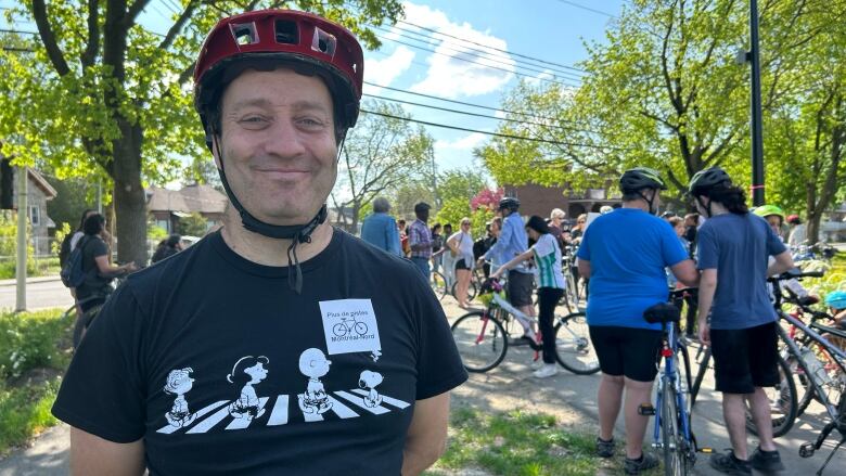 A man wearing a bicycle helmet smiles at the camera, with many cyclists pictured around him. 