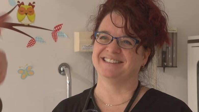 A woman with glasses and a stethescope arround her neck smiles at the camera. 