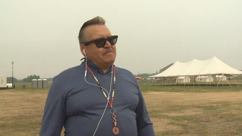 A man stands in a field with tents behind him.