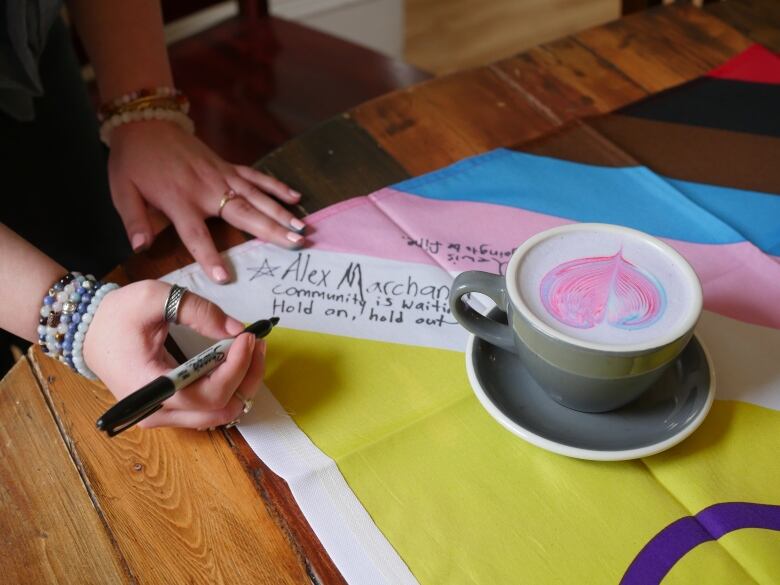 A hand holding a sharpie signs a pride flag. 