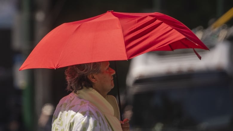 A woman with grey hair holds an umbrella to protect her from the sun in Vancouver.