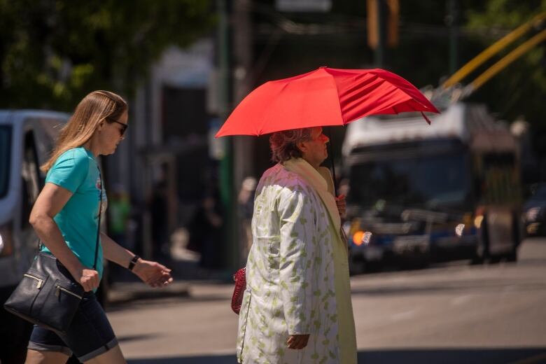 A woman with grey hair holds an umbrella to protect her from the sun in Vancouver.