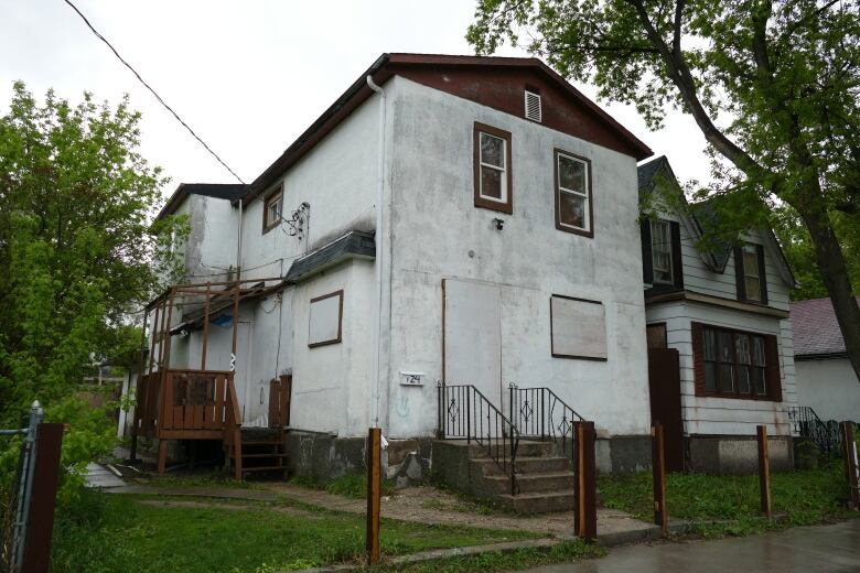 A white two-storey house with boarded up windows. 