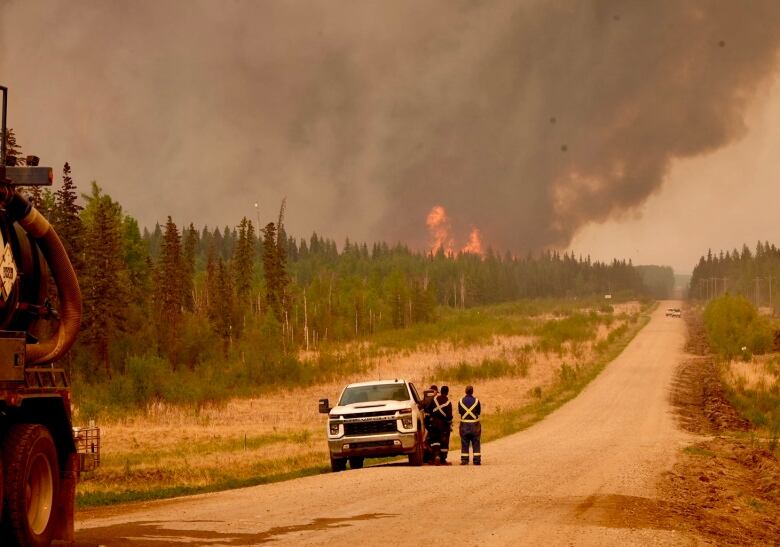 Three people look at a fire burning in the distance.