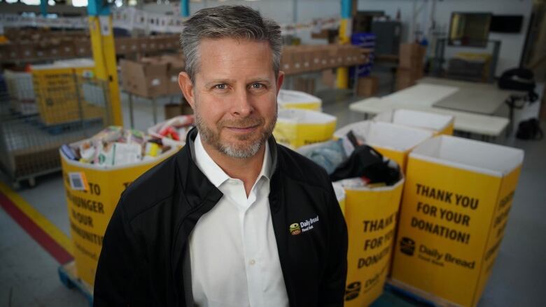 Man in a black coat standing in front of bins full of donated food.