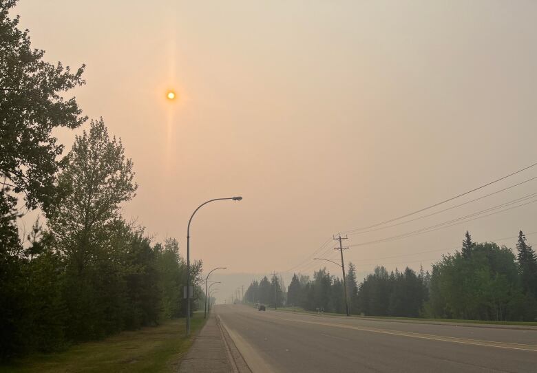 Vehicles travel on a road with the sun in the sky peeking through a hazy sky.