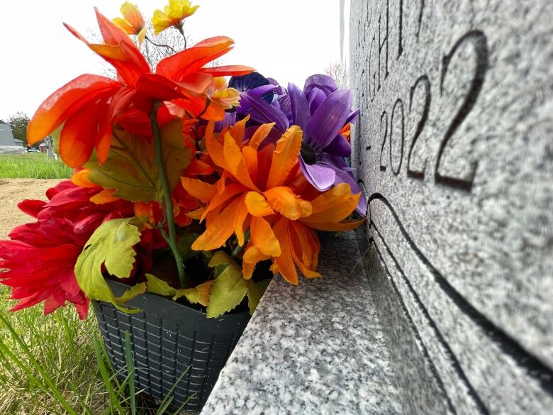 A partial view of a gravestone with a small basket of fake flowers in front of it