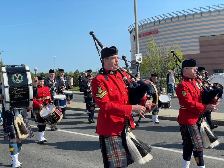 Bagpipers in red pass a hockey arena.