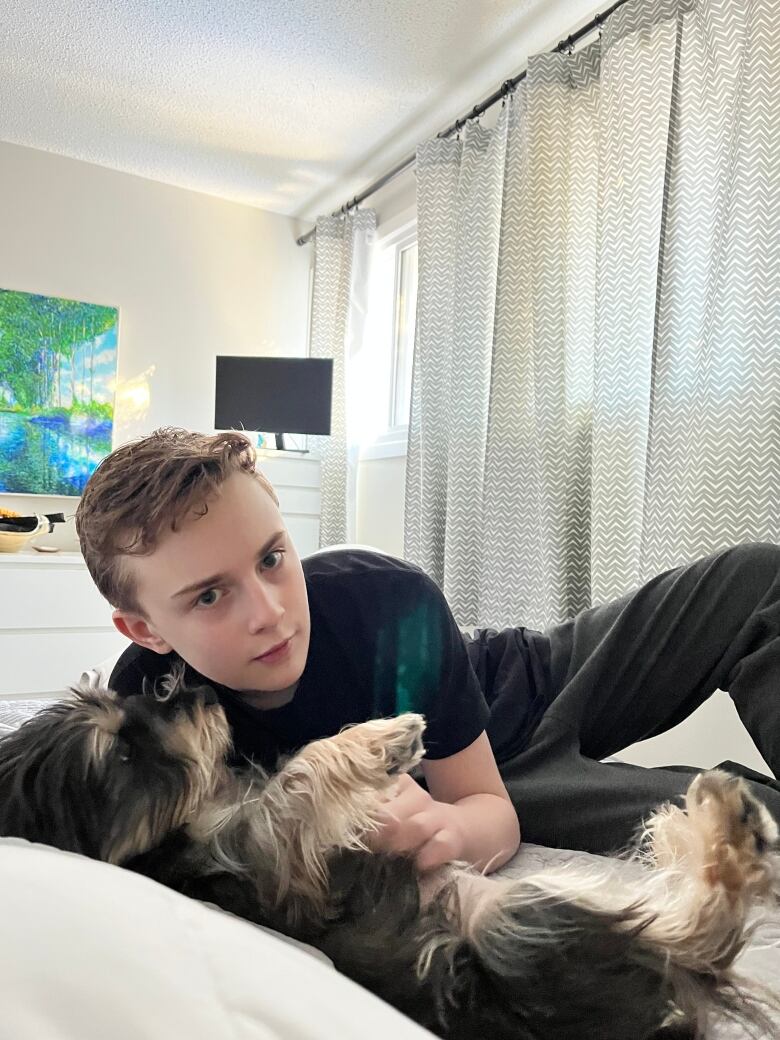 A  boy can be seen lying on a bed with a small dog.