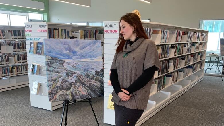 Artist Hanna Furs is pictured with the first painting she made upon arriving in Newfoundland last year. It's an acrylic painting of a rocky beach. 