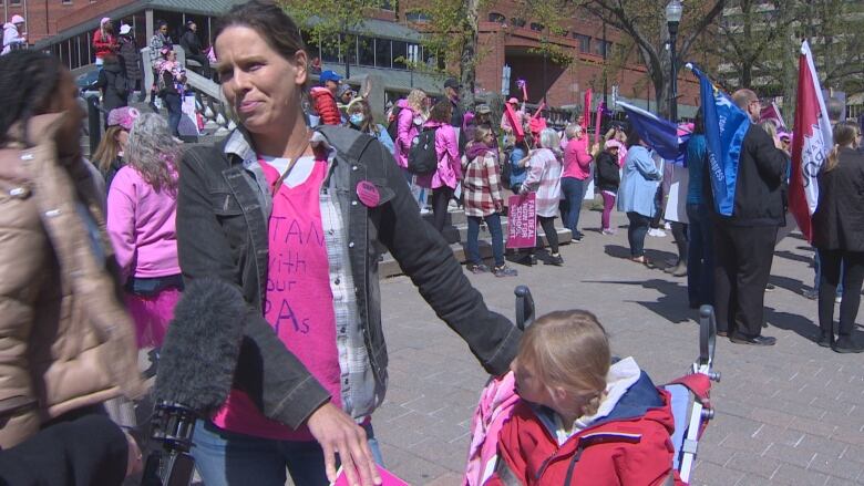 A woman in a pink T-shirt stands alongside her daughter as demonstrators with flags and placards mill around in the background.