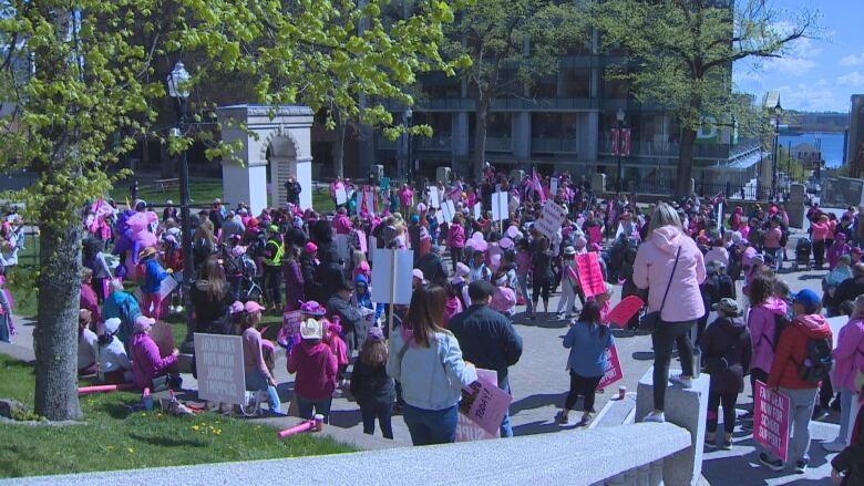 A large crowd, many dressed in pink, stands in a public square with balloons and placards.