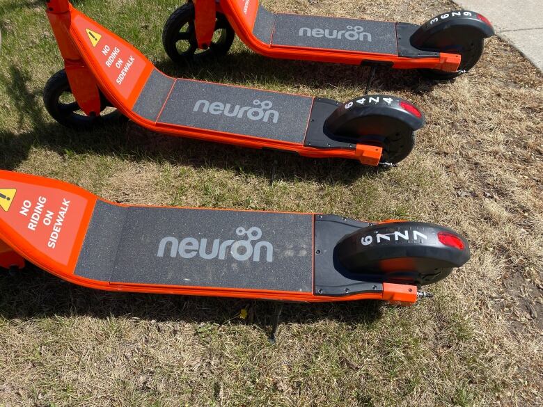 Three neuron e-scooters are on grass 