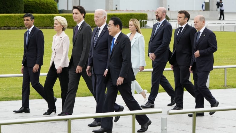 A group of people, all G7 leaders, walk along a sidewalk in a park.