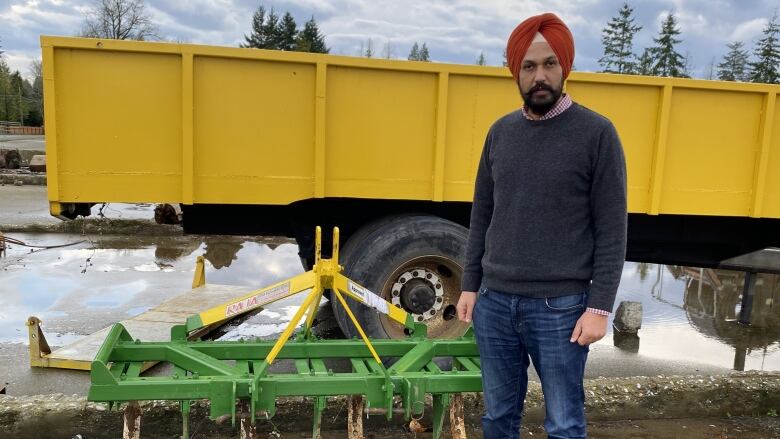 A man is pictured next to his farming equipment, a green cultivator, in front of a yellow truck.