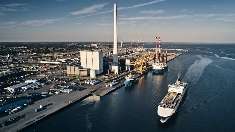 A port with wind turbines in the background and a boat on the water.