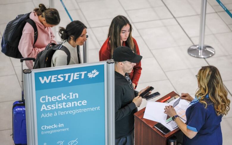 Several people line up to speak to a woman at an airport kiosk.