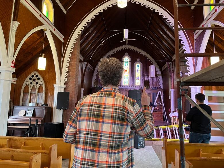 A man stands next to scaffolding in an old church pointing up. 