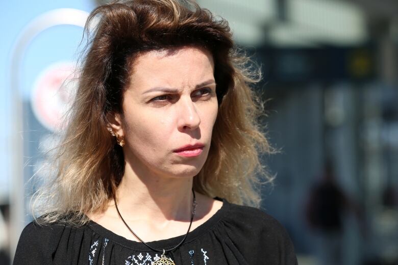 A woman with dirty blond hair stands outside an airport.