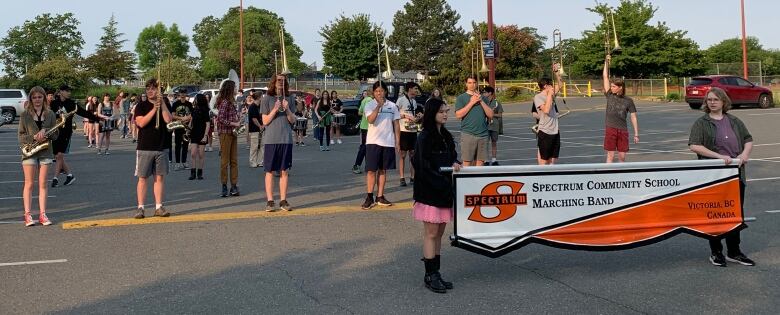 A group of students rehearse marching band in a parking lot. 