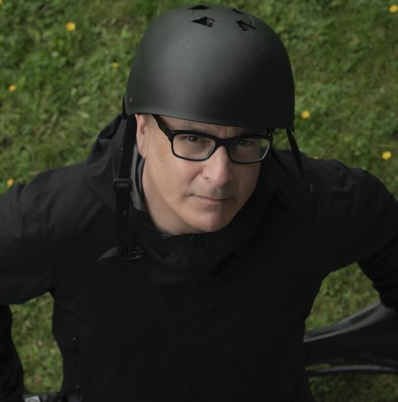 A man dressed in all black stands with a bike helmet