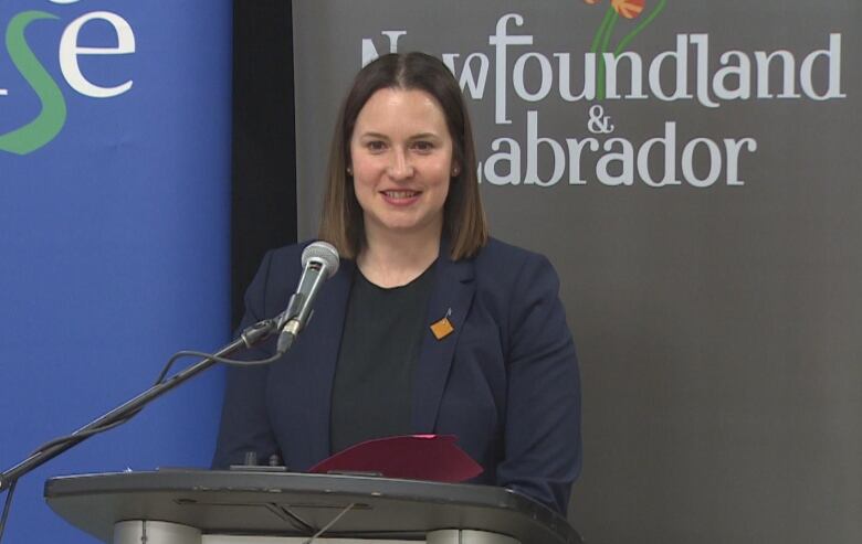 A white woman with brown hair wearing a blue blazer and a black t-shirt.