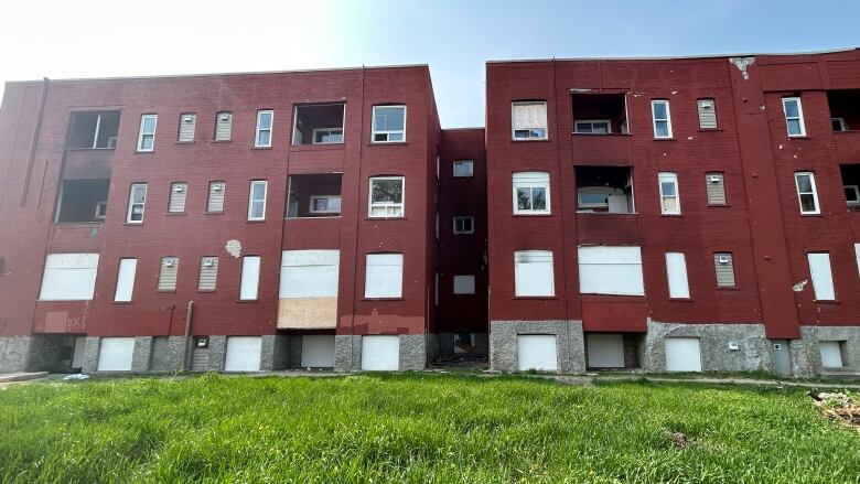 The side view of a large apartment building, boarded up on the lower two levels.